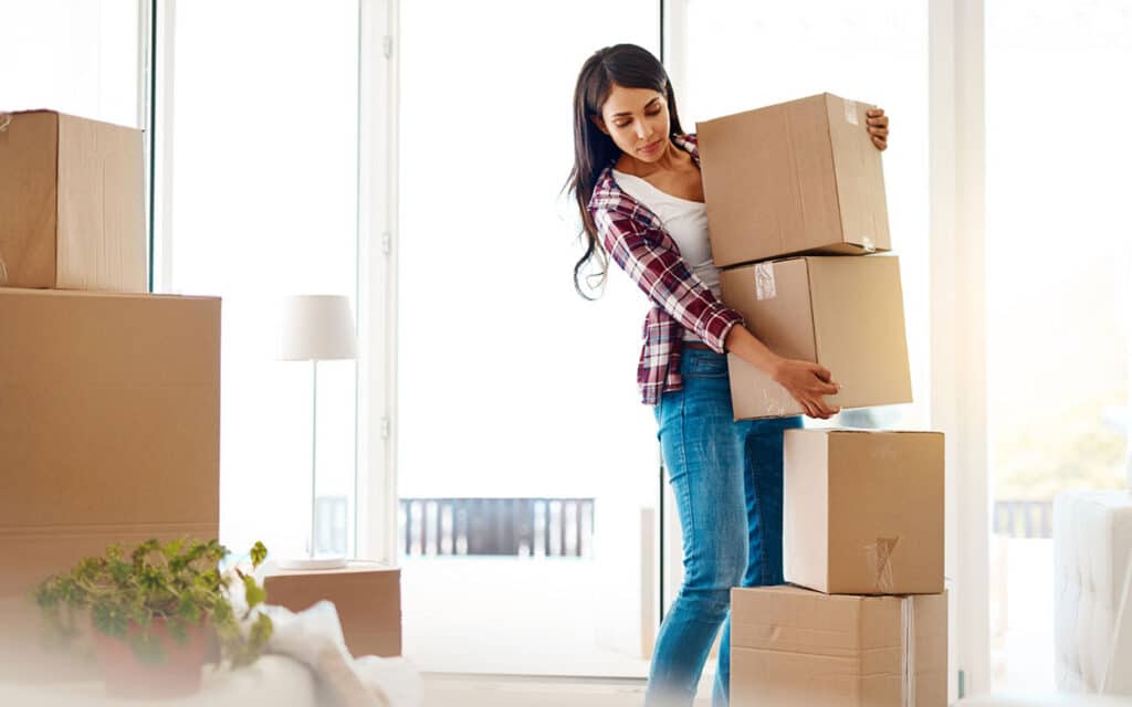 A woman wearing a plaid shirt and jeans stacks cardboard boxes
