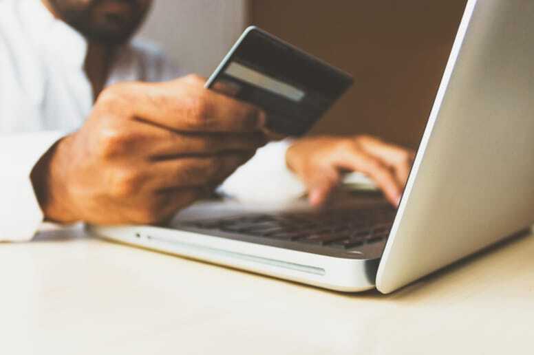 A person holds a credit card in their right hand while typing on a laptop keyboard with their left hand.