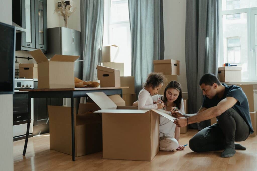 A family unpacks boxes in a sunlit kitchen area.