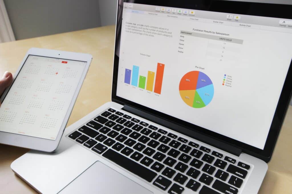 A person holds a tablet displaying a calendar next to an open laptop showing charts, graphs, and data on the screen.