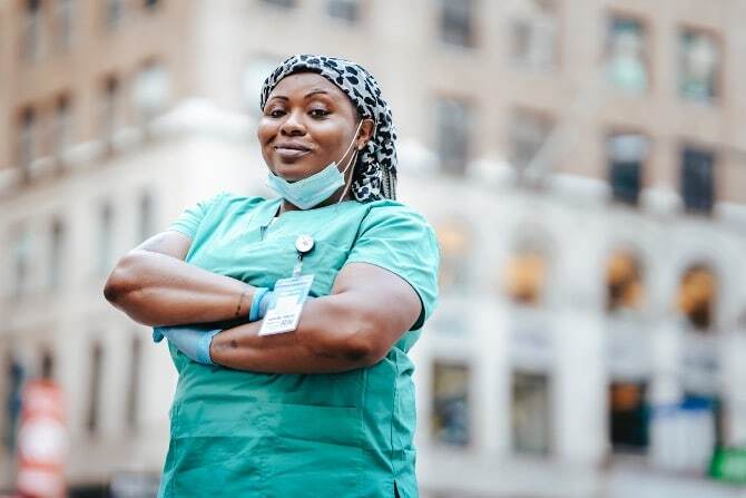 A healthcare worker in green scrubs stands with arms crossed