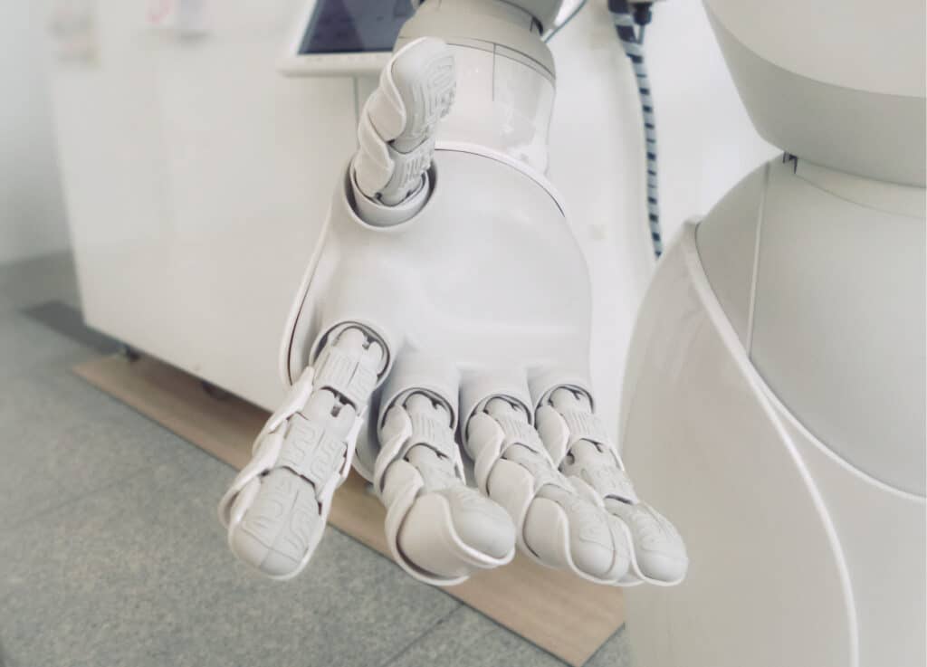 A close-up of a white robotic hand with articulated fingers, demonstrating advanced mechanical design in a tech lab setting.