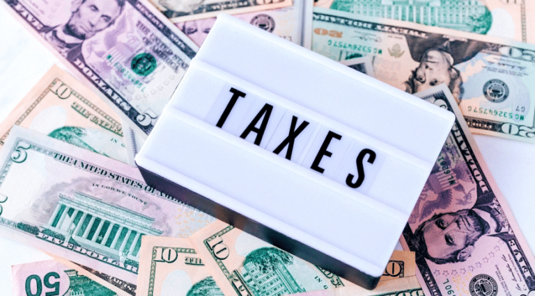 A sign displaying the word "TAXES" sits on a spread of various U.S. dollar bills.