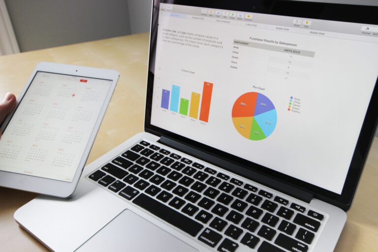 A person holds a tablet displaying a calendar next to an open laptop showing charts, graphs, and data on the screen.