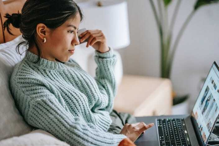 A person in a green sweater sits on a couch using a laptop, looking at the screen attentively.