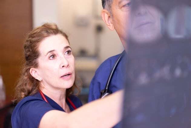 Two healthcare professionals in blue scrubs examine an X-ray, with one pointing at a specific area on the film.